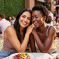 Two women smiling and enjoying a meal together outdoors.