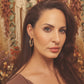 Woman with long brown hair and hoop earrings against a neutral background